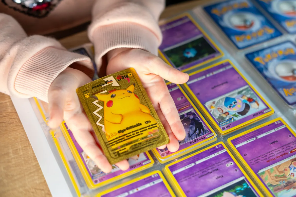 A child holding a gold Pikachu card over a binder of Pokémon cards