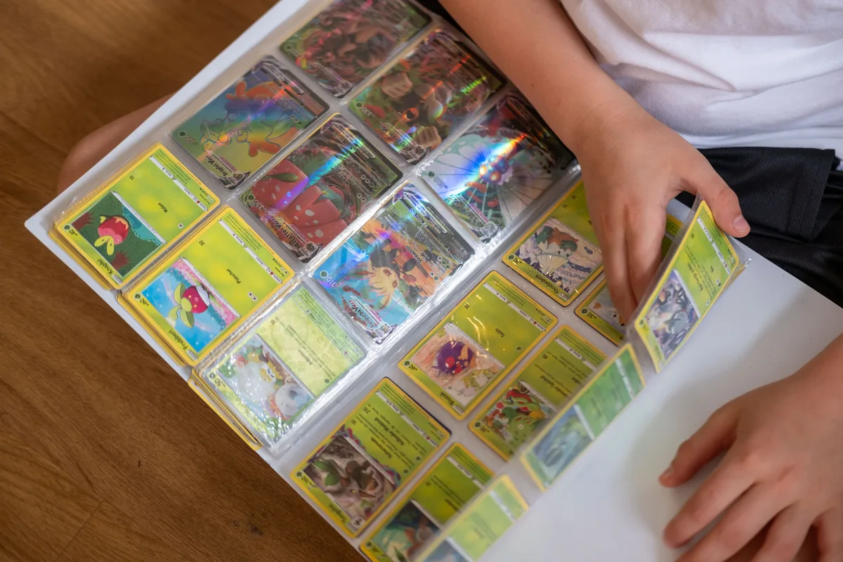 A binder of holo Pokémon cards open on a child's lap